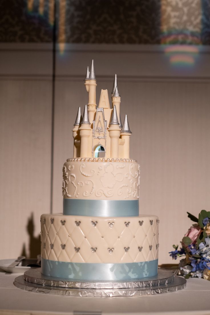 a wedding cake with a castle on top and blue ribbon around the edges is sitting on a table