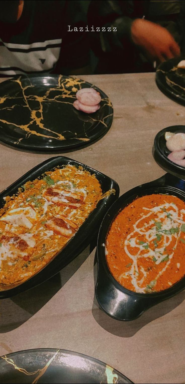 several different types of food in black pans on a table with plates and utensils