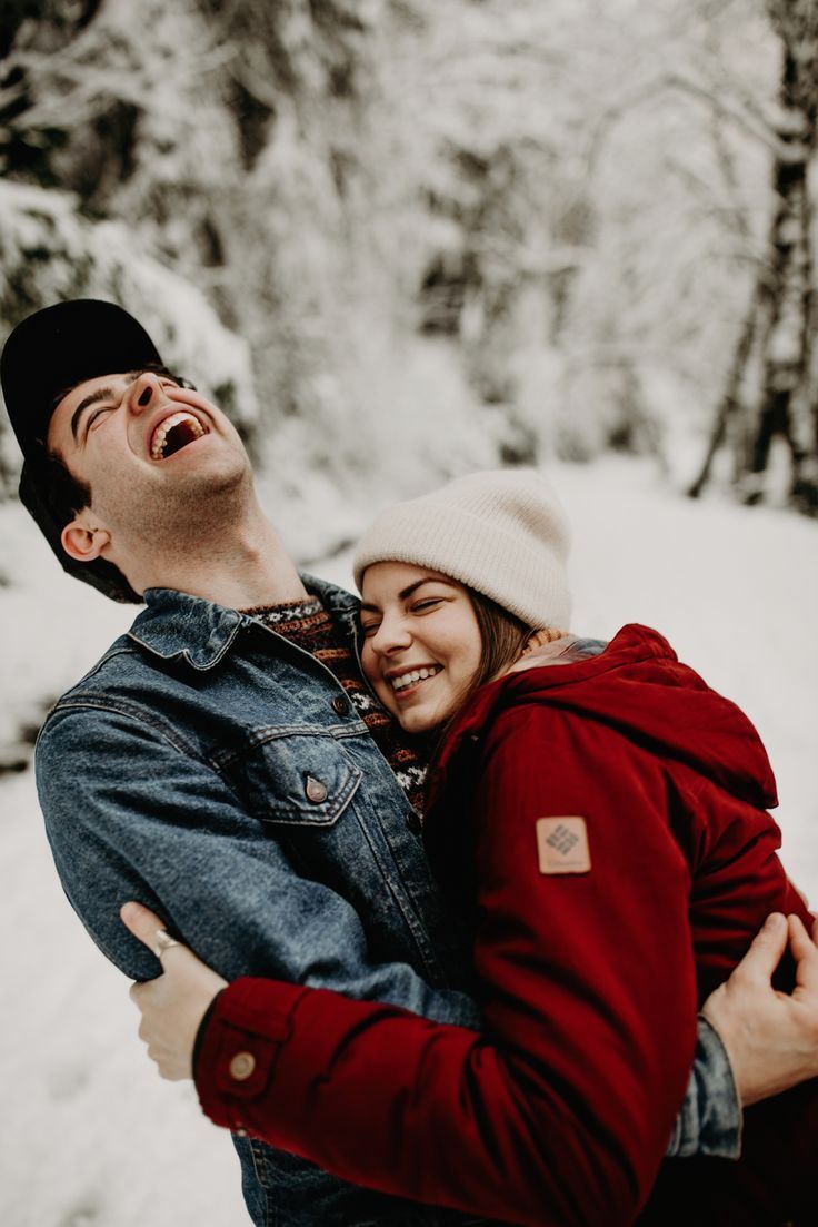 a man and woman are laughing together in the snow while holding each other's arms