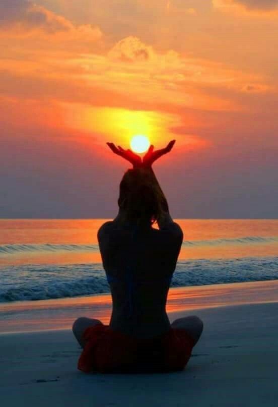 a person sitting on the beach with their hands up in the air as the sun sets