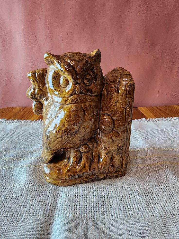 an owl figurine sitting on top of a white table cloth next to a pink wall