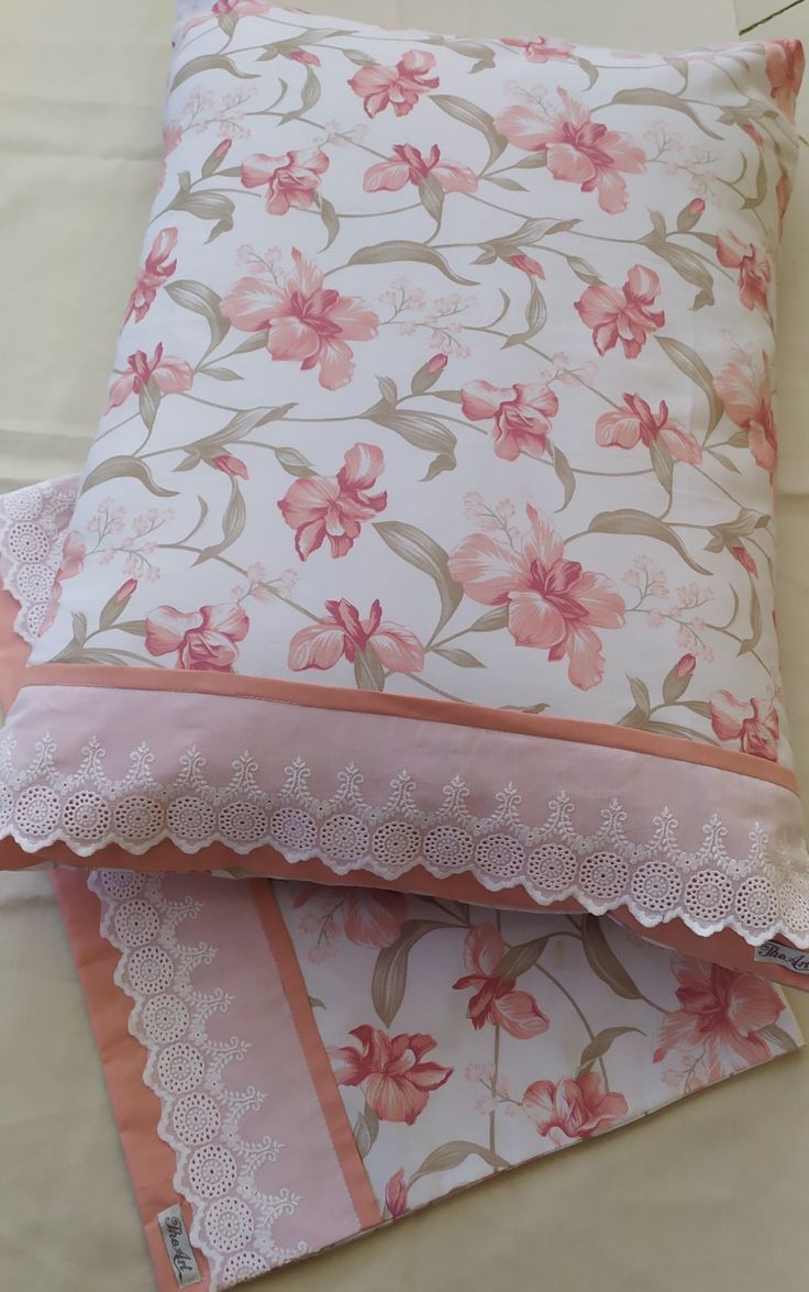 two pillows with pink flowers and lace trims sitting on top of each other in front of a white wall