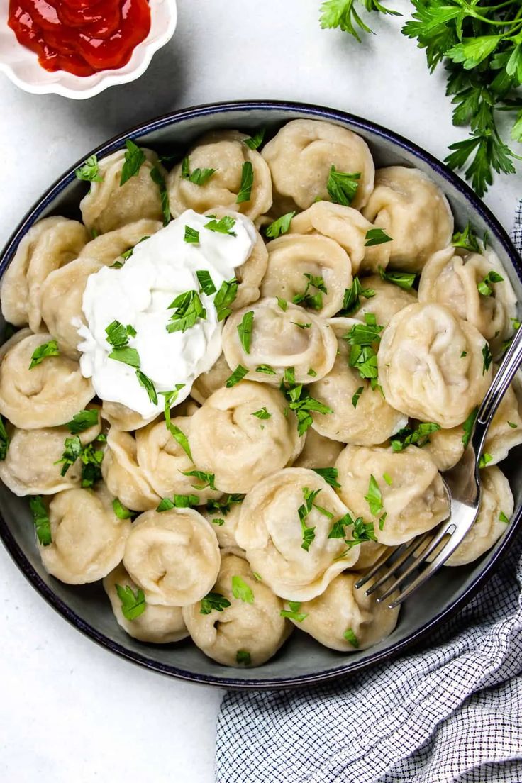 a bowl full of dumplings with sour cream and parsley on the side next to some ketchup