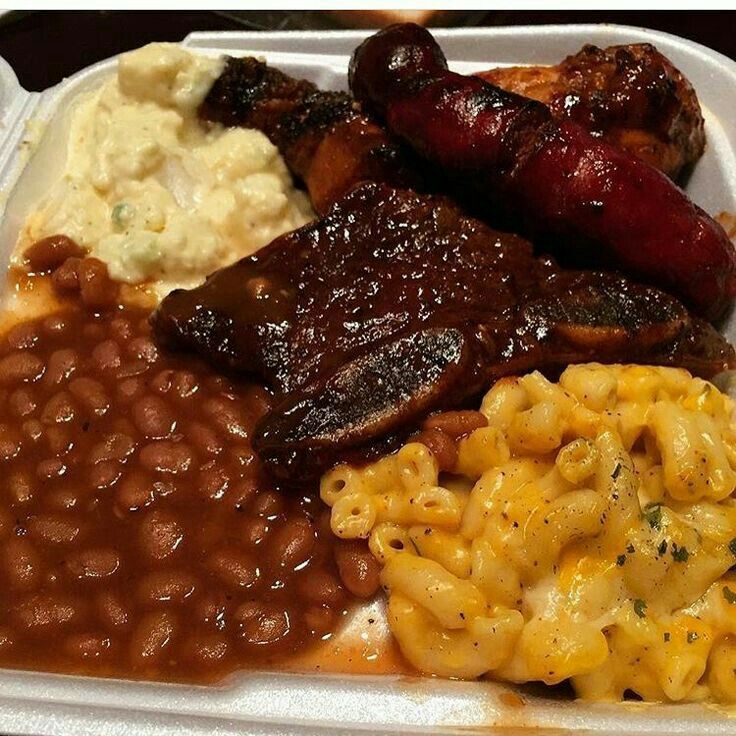 a white takeout container filled with beans, macaroni and cheese and sausage