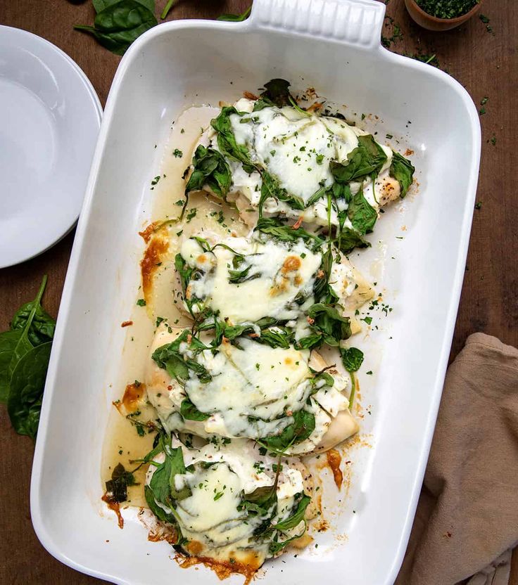 a casserole dish with spinach, cheese and sauce in it on a wooden table