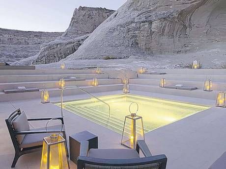 an outdoor pool surrounded by chairs and lights in the middle of a desert area with mountains in the background