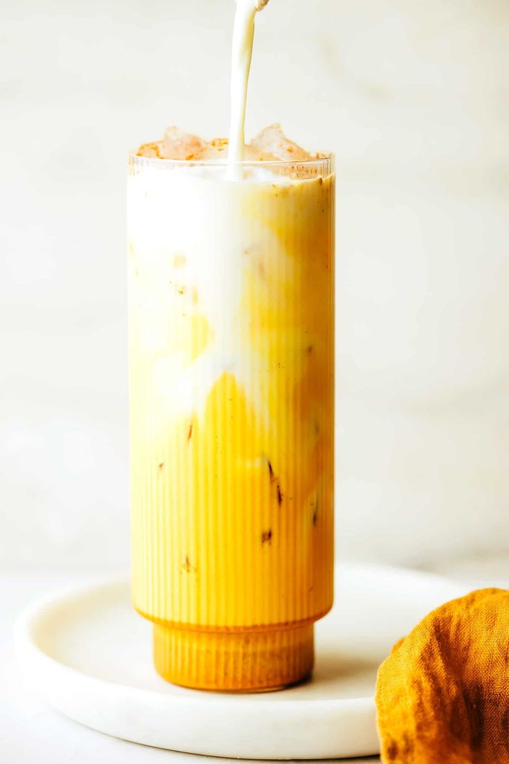 a drink being poured into a glass on a plate with a donut next to it