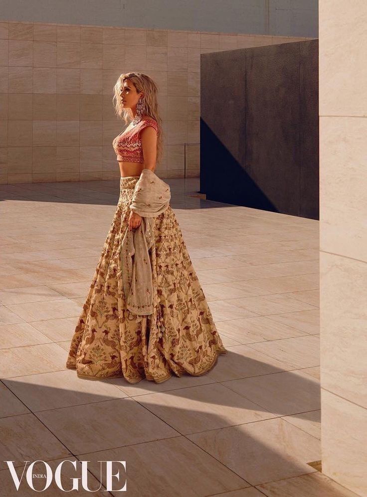 a woman in a long skirt and crop top standing on a tile floor next to a wall