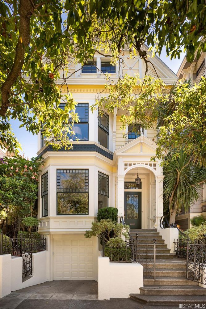 a large white house with stairs leading up to the front door and trees in front of it