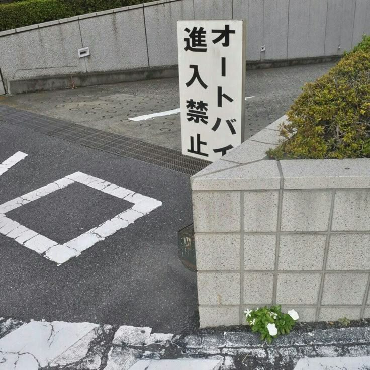 an empty parking lot with a sign in the middle and flowers growing out of it