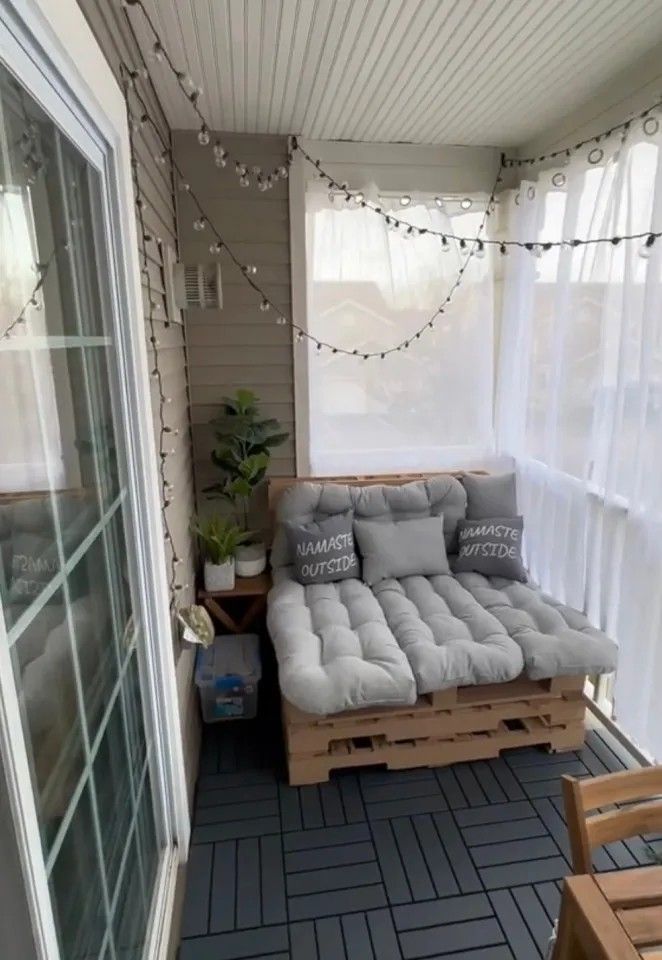 a couch sitting on top of a wooden pallet next to a glass door with string lights