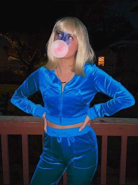 a woman with blonde hair and blue clothes blowing a bubble into her mouth while standing on a deck