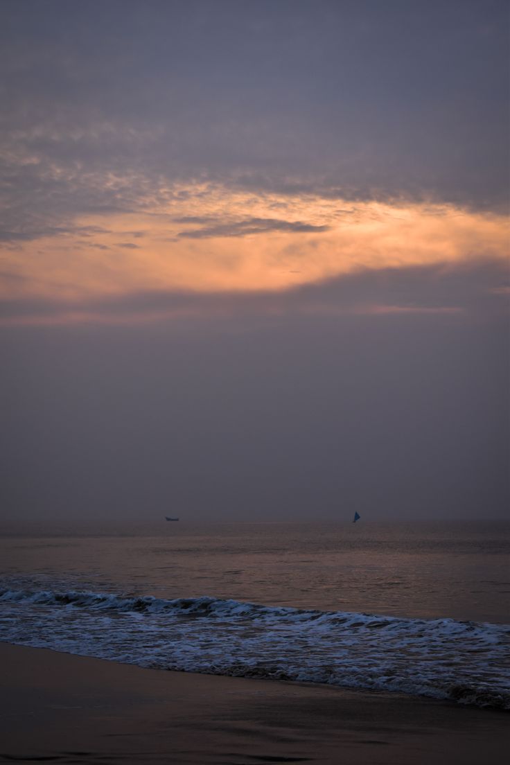 the sun is setting over the ocean with a boat in the distance