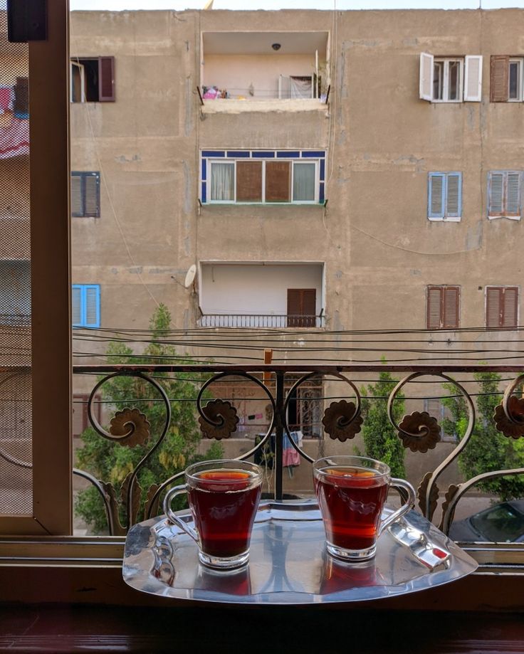 two glasses of tea sit on a tray in front of a window overlooking an apartment building