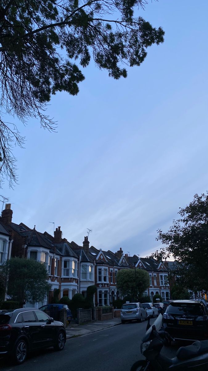 cars are parked on the street in front of some houses at dusk with blue skies