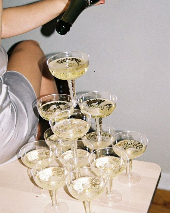 a woman pouring champagne into wine glasses on top of a wooden table in front of a white wall