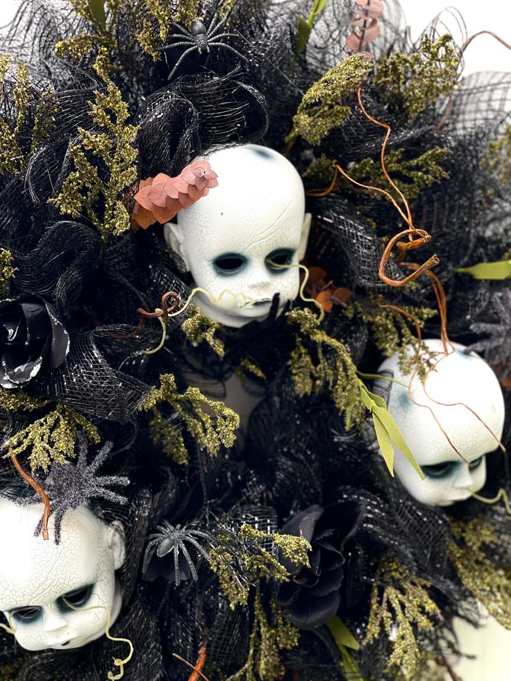 three white dolls with black and green decorations on their heads are sitting in a wreath