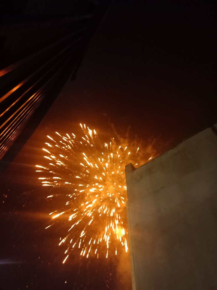 fireworks are lit up in the night sky above a building and street lights, as seen from below