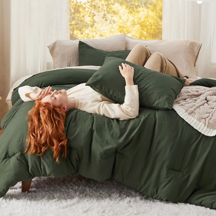 a woman laying on top of a bed covered in green comforter and pillow cases