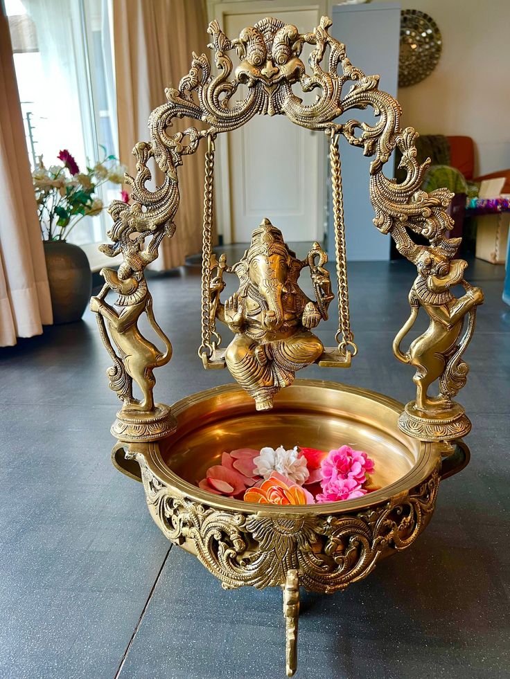 a gold plate with flowers in it on the floor next to a mirror and potted plant