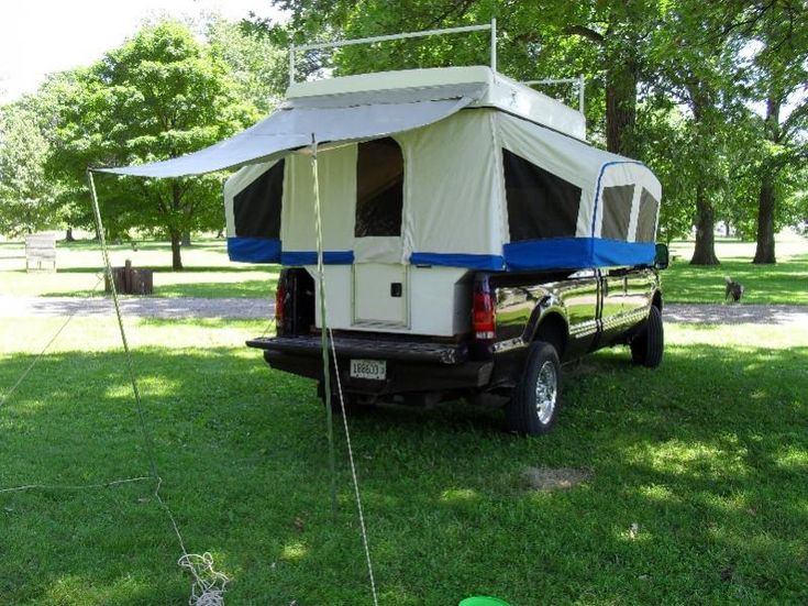 a truck with a tent attached to it parked on the grass in front of trees