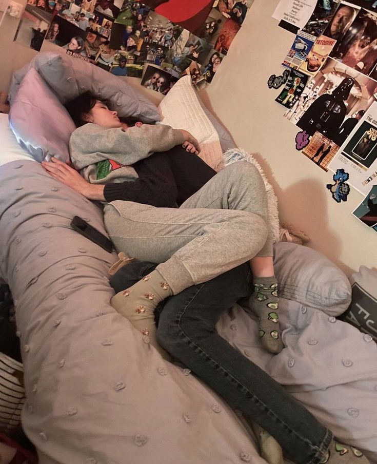 two people laying on top of a bed covered in pillows