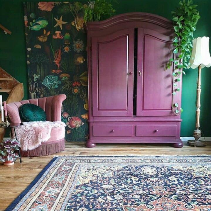 a pink arm chair sitting next to a purple cabinet in a room with green walls