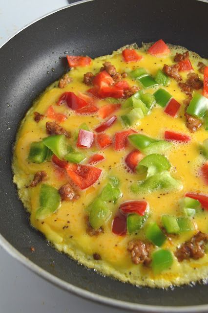 an omelet with sausage, peppers and cheese in a pan on the stove