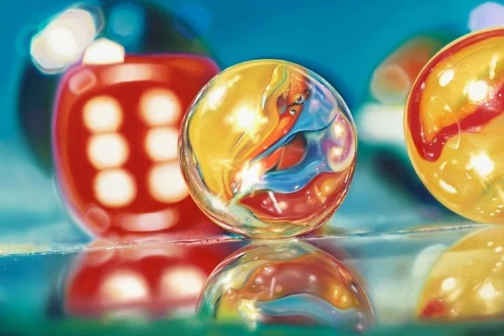 two colorful glass balls sitting next to each other on top of a reflective surface with lights in the background