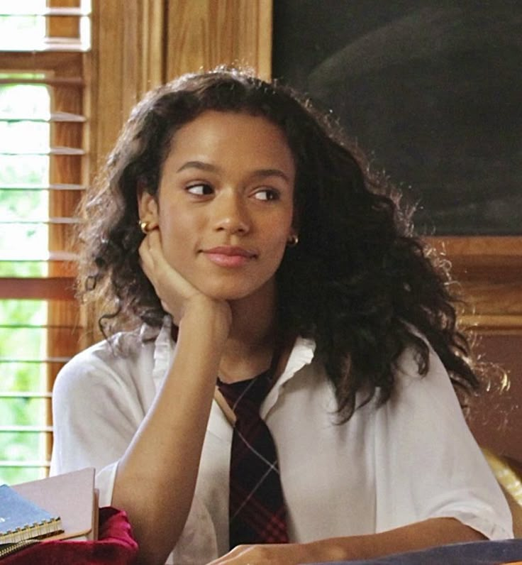 a young woman sitting at a desk in front of a blackboard