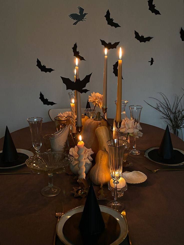 a dining room table with candles and halloween decorations on it, bats are flying overhead