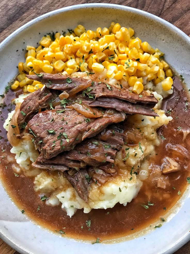 a white plate topped with meat and mashed potatoes on top of a wooden table