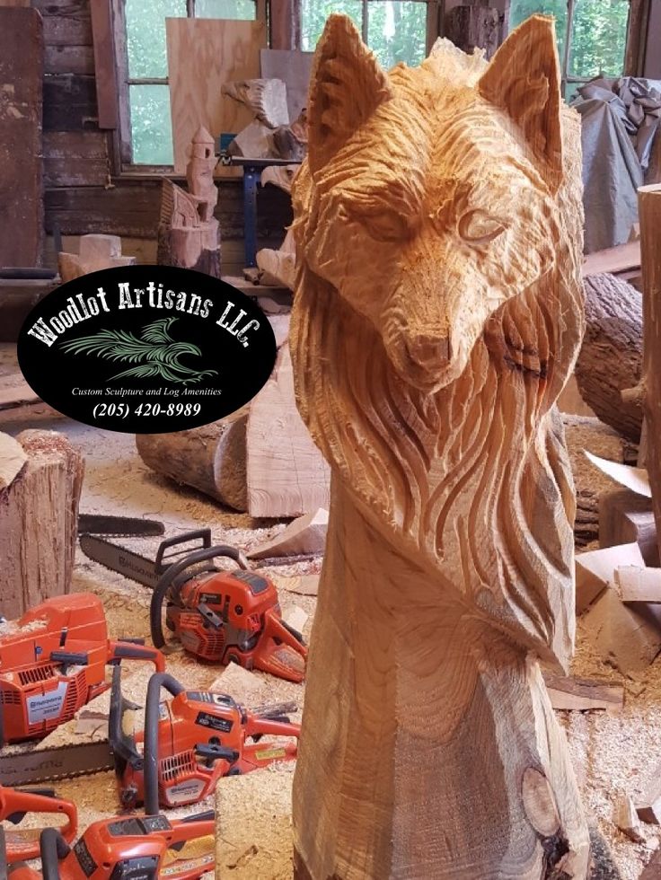 a wooden carving of a wolf with chainsaws on the ground next to it