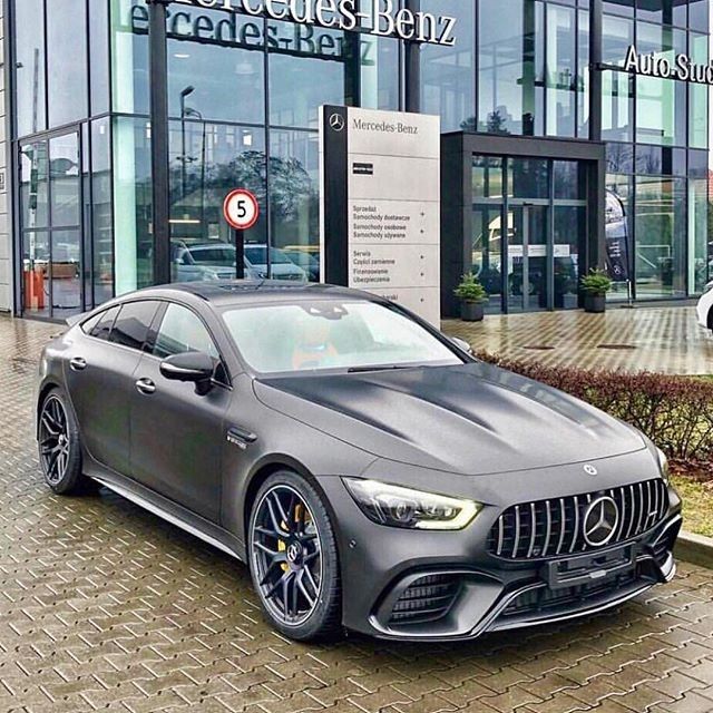 a grey mercedes benz is parked in front of a car dealership on a rainy day