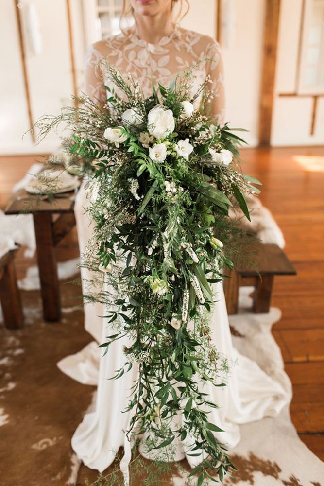 a bridal holding a bouquet of flowers and greenery in front of a wooden table