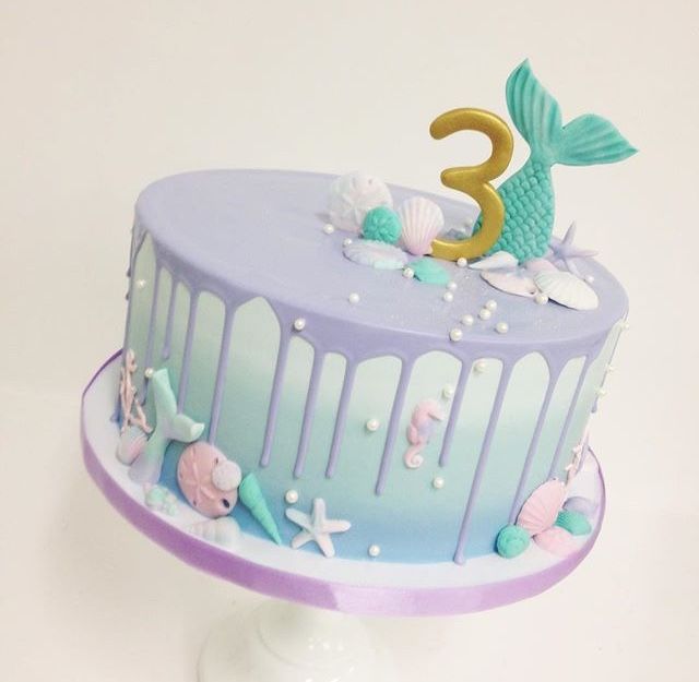 there is a blue and purple cake with mermaid decorations on the top, along with other sea creatures