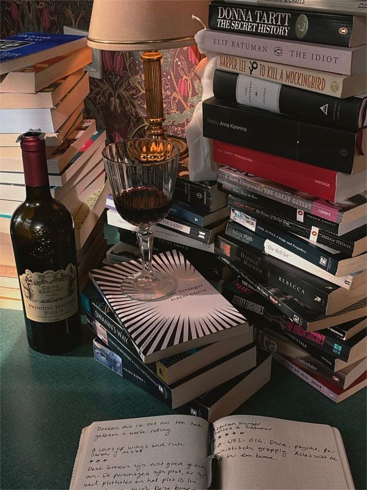 a table topped with lots of books and a bottle of wine next to a lamp