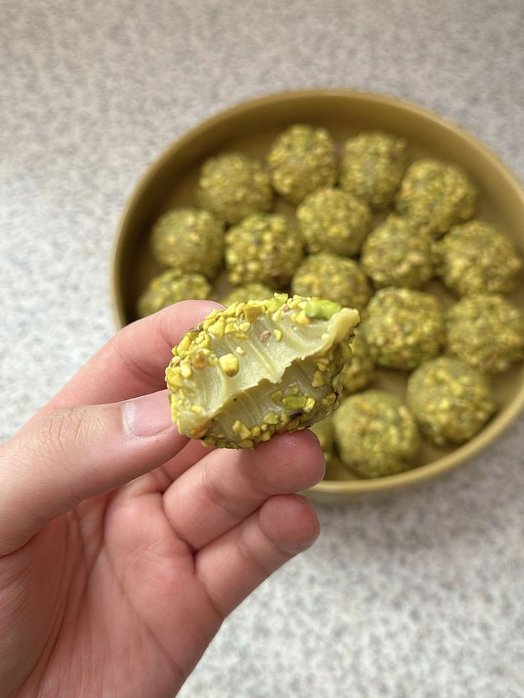 a hand holding a piece of broccoli in front of a bowl of food