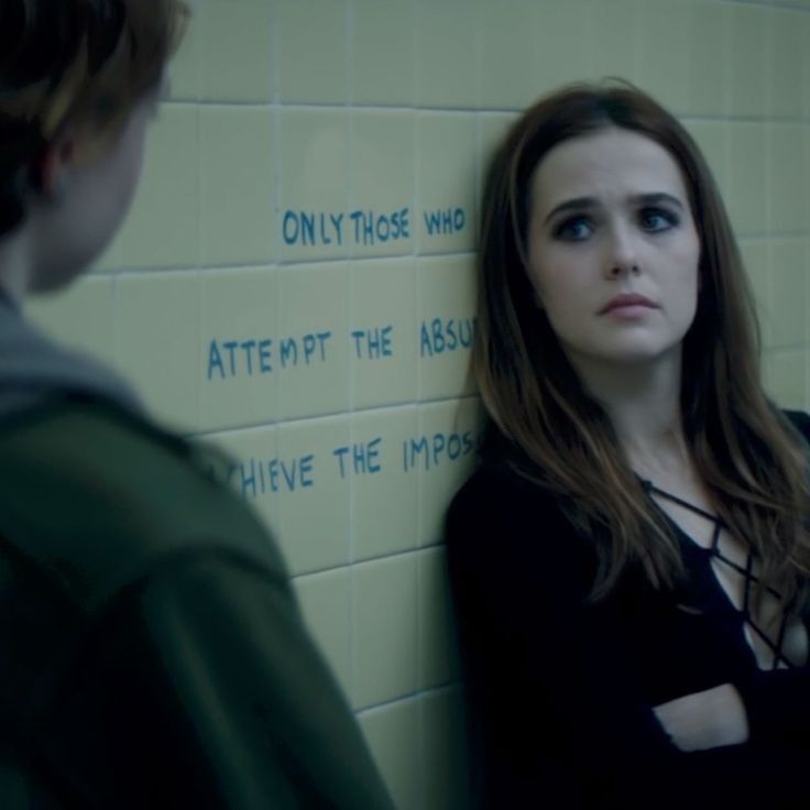 a woman standing in front of a wall with writing on it and another person looking at her