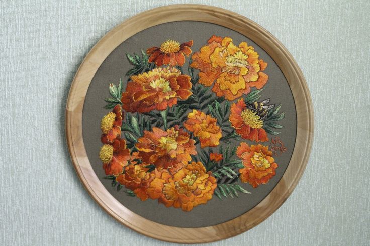 an embroidery project with orange and yellow flowers in a wooden frame on a blue wall