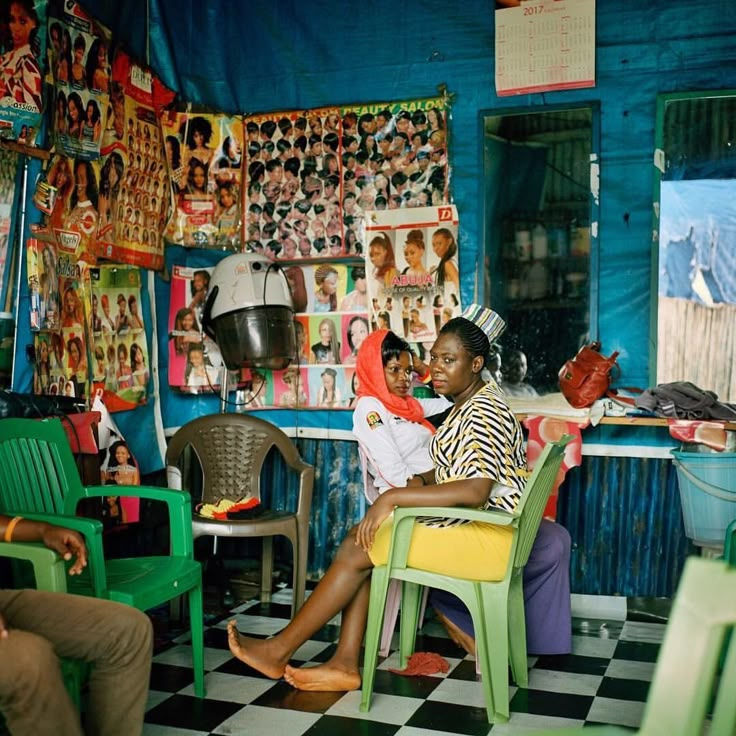 two people sitting in chairs at a barbershop with posters on the wall behind them