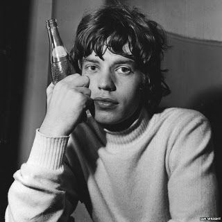 black and white photograph of a man holding a beer in front of his face while talking on the phone