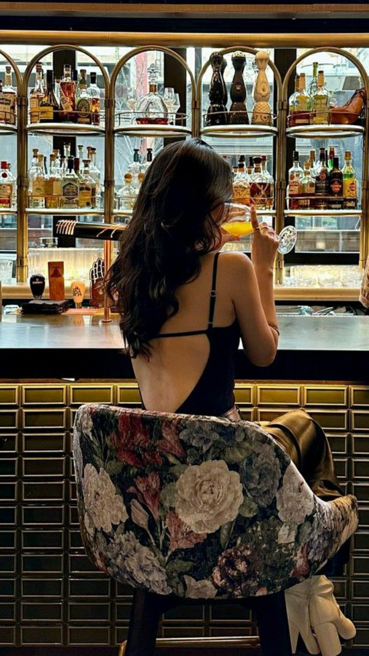 a woman sitting at a bar drinking from a wine glass in front of the bar