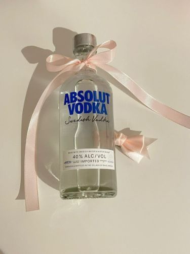 a bottle of absolut vodka with a pink ribbon around it on a white surface