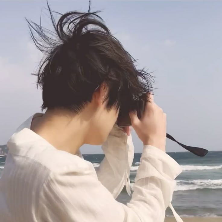 a person standing on the beach with their hair blowing in the wind and looking at the ocean