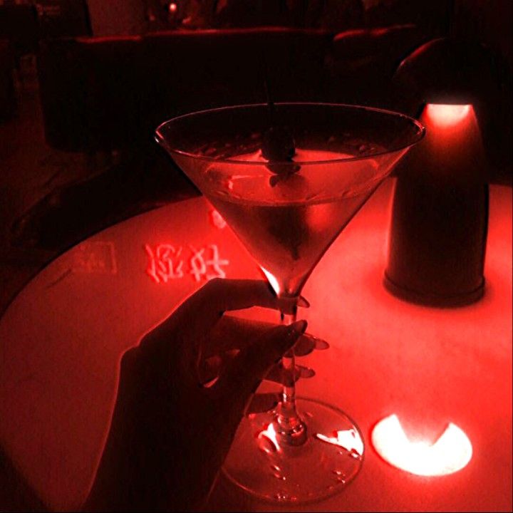 a person is holding a martini glass in front of a lit candle on a table