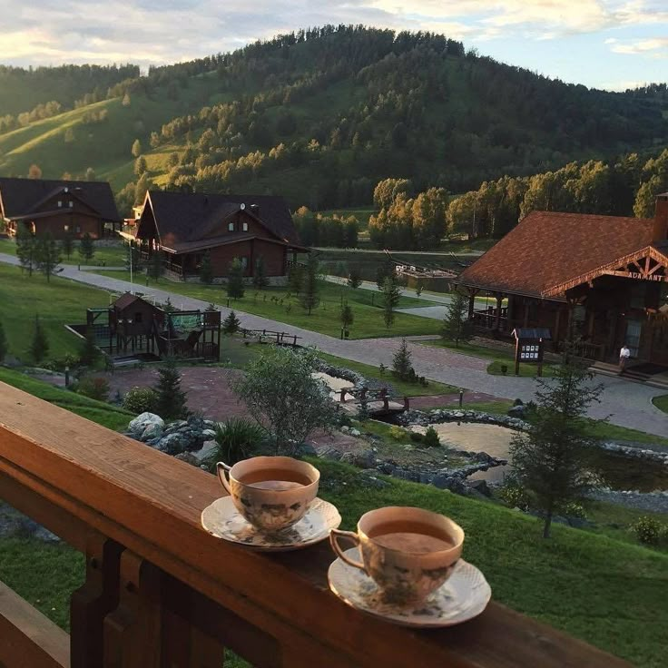 two cups of coffee sit on a balcony overlooking a scenic area with mountains in the background