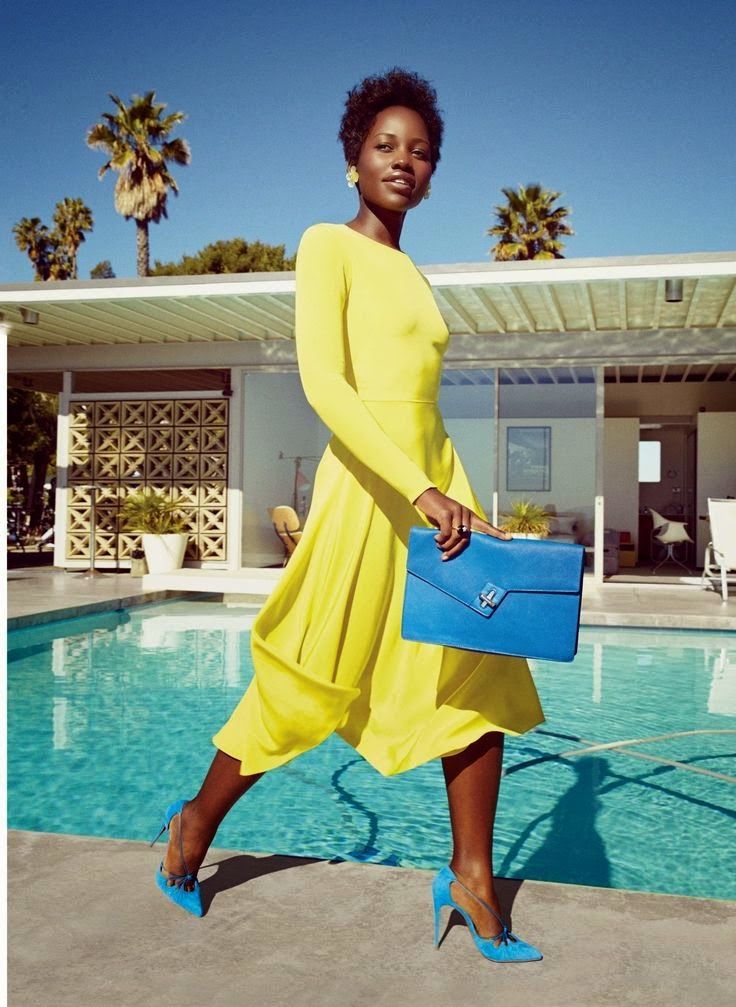 a woman in a yellow dress is holding a blue purse near a pool with palm trees