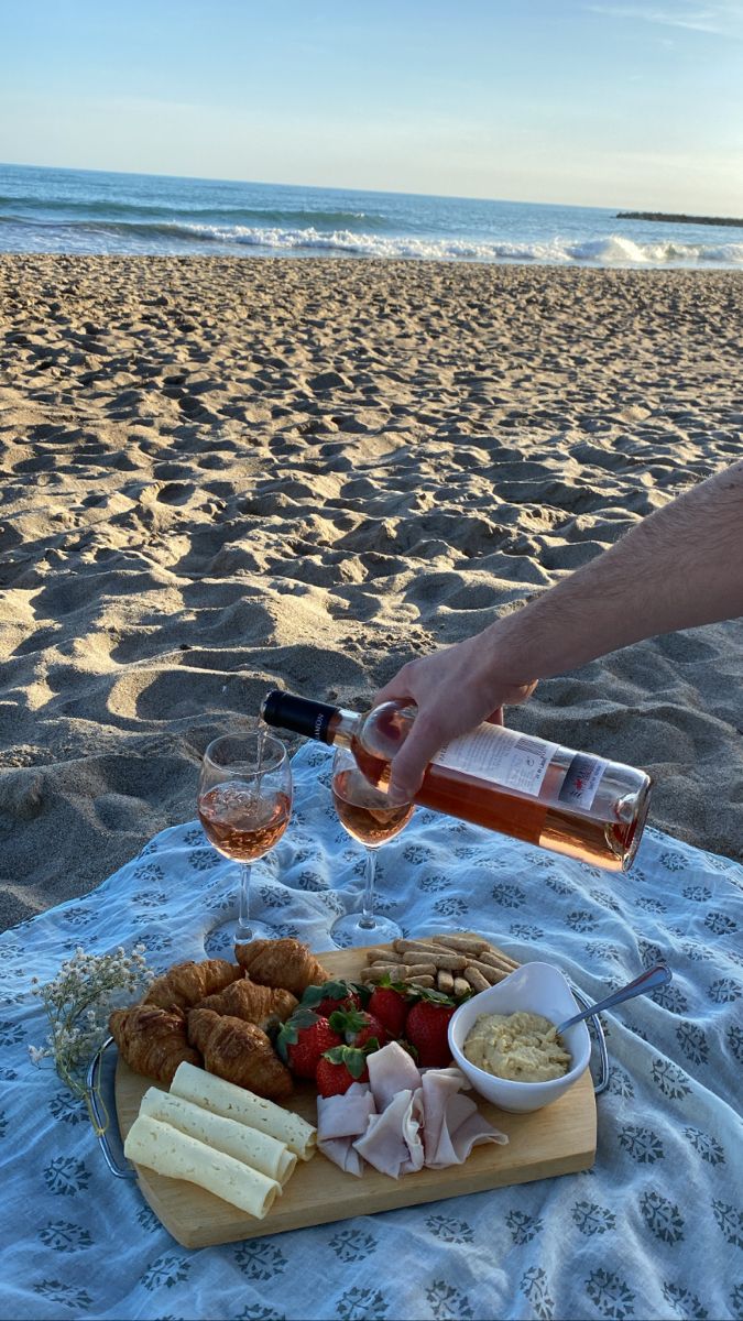 a person pouring wine into a glass at the beach with food and drinks on it