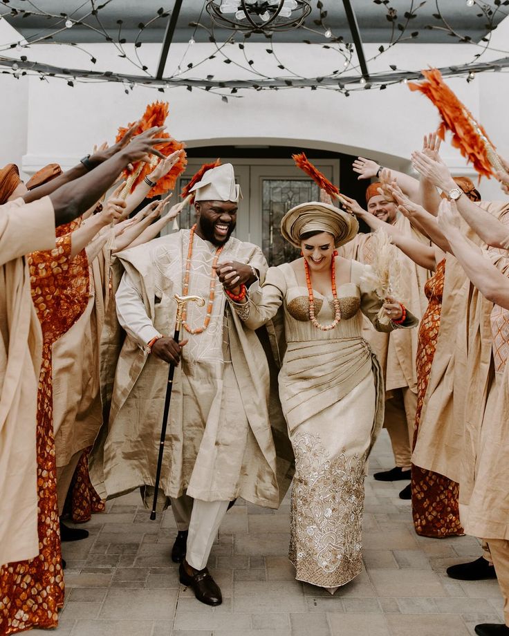 a man and woman walking through a group of other people with orange garlands on their heads